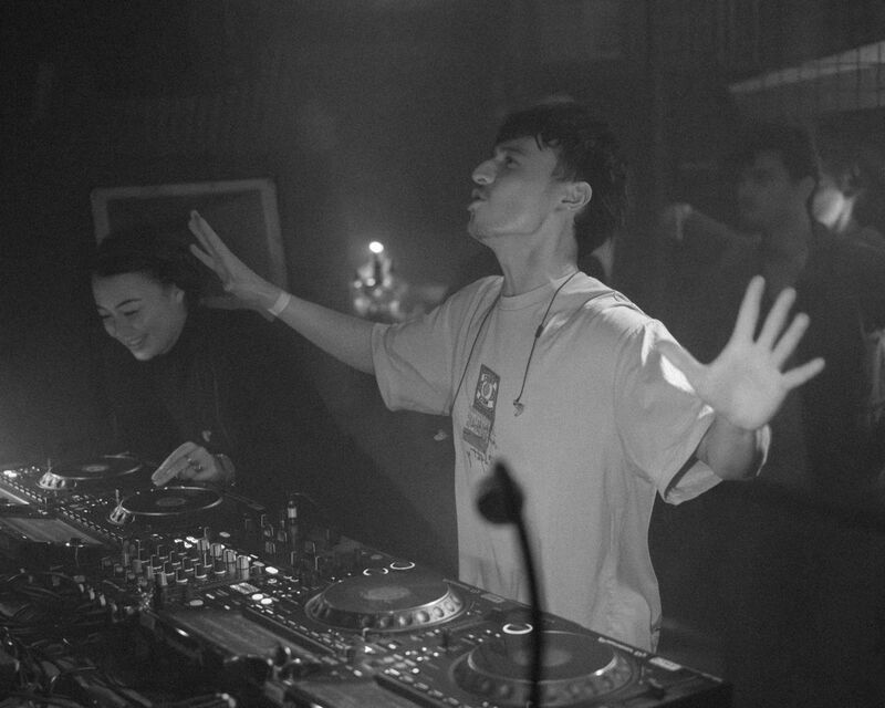 Demi and Robin with hands raised behind the decks, crowd energy