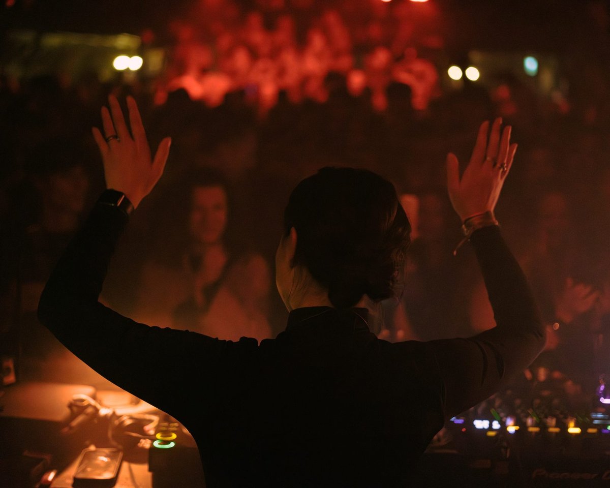 Demi Drabe with hands raised, crowd bathed in red light