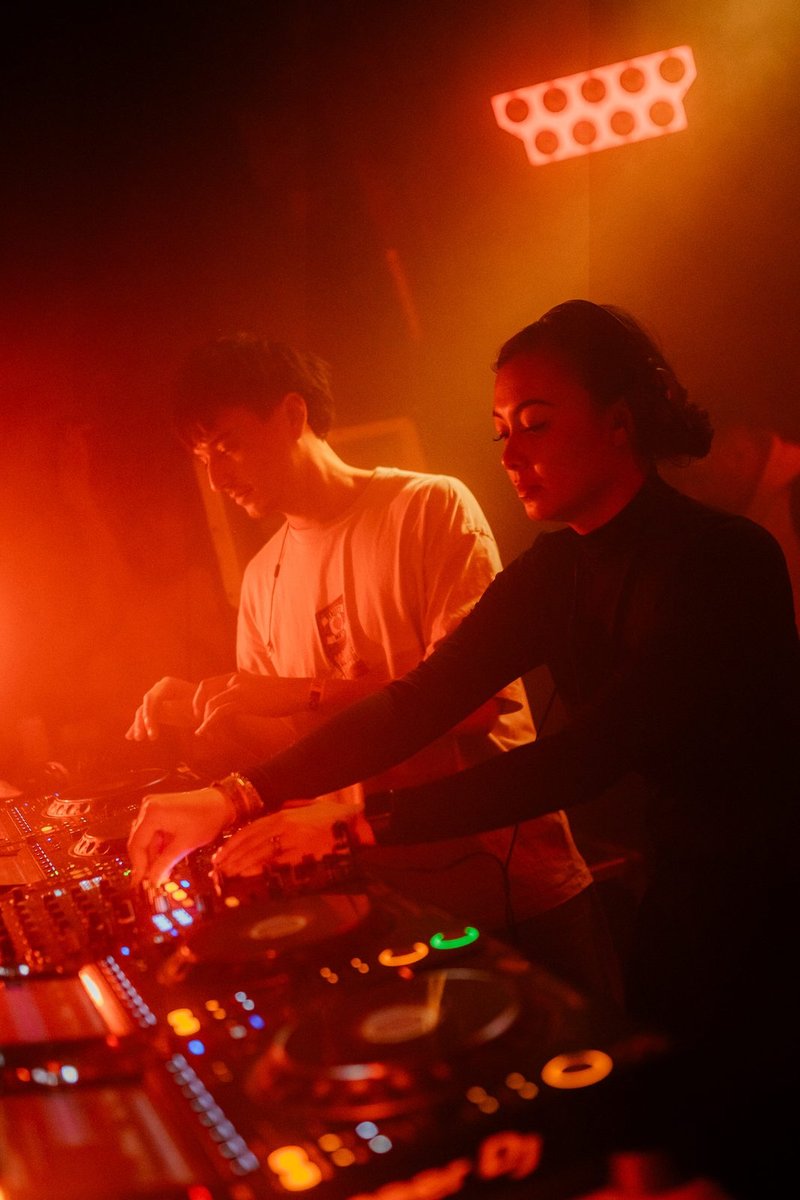 Demi and Robin behind the decks at Thuishaven, warm red and orange lighting